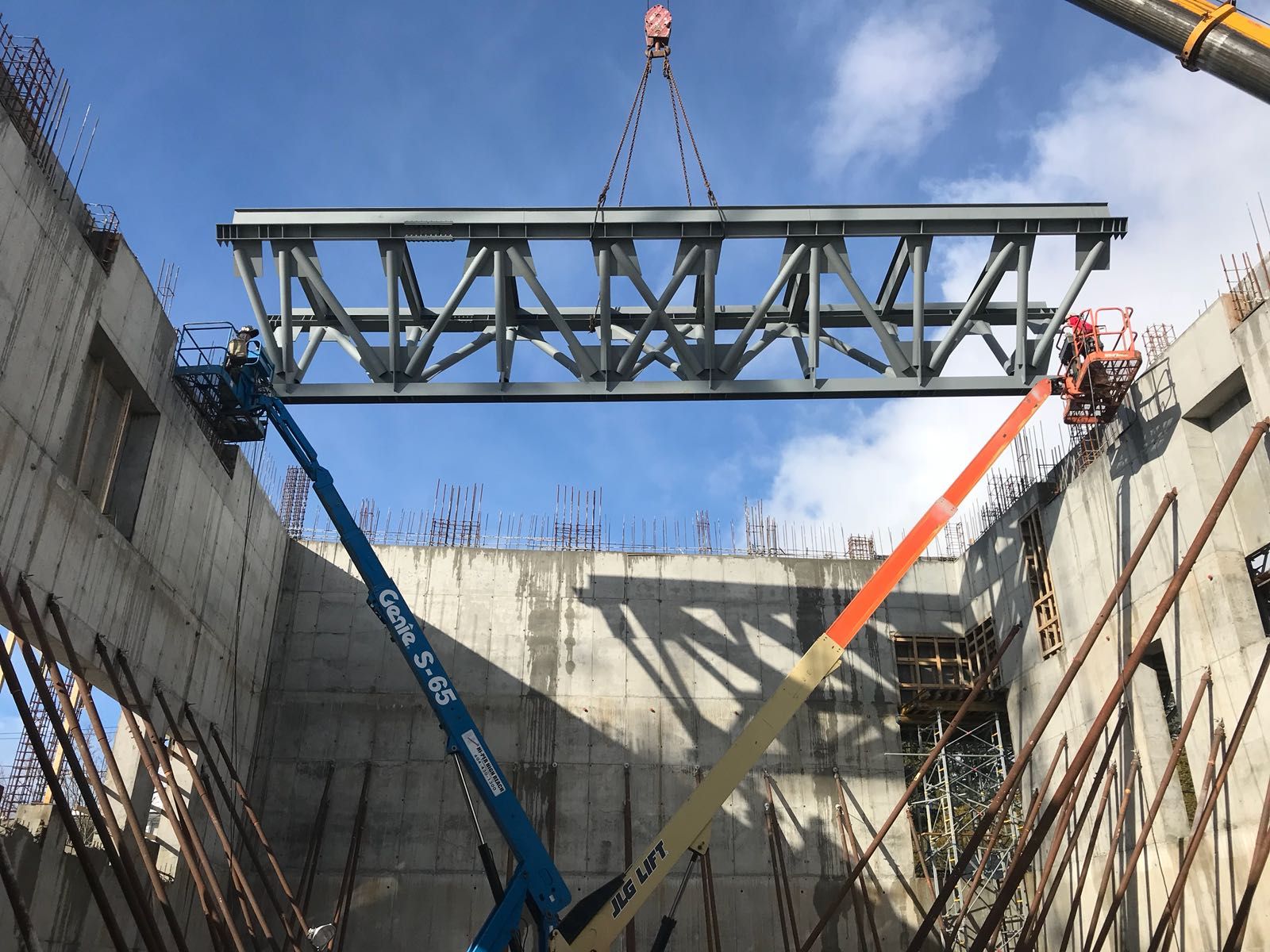 A large structural steel truss craned into place against a clear blue sky